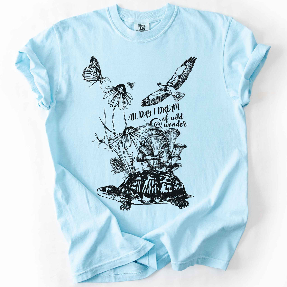 Chambray "Fauna and Flora" t-shirt on Comfort Colors tee, featuring the words "all day I dream of wild wonder", and a nature scene in black line art style with a box turtle, mushrooms, wildflowers, a hawk, a butterfly, and a snail. Nature lover and forager gift shirt for cottagecore and wildlife enthusiasts.