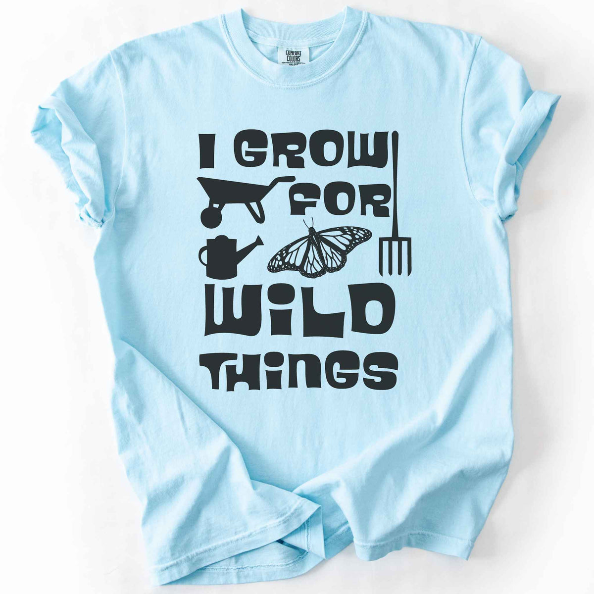 Chambray "I Grow for Wild Things" t-shirt on Comfort Colors tee, featuring a monarch butterfly with garden tool icons and bold black lettering text. Gardener and native plant gift shirt for pollinator conservation fans.