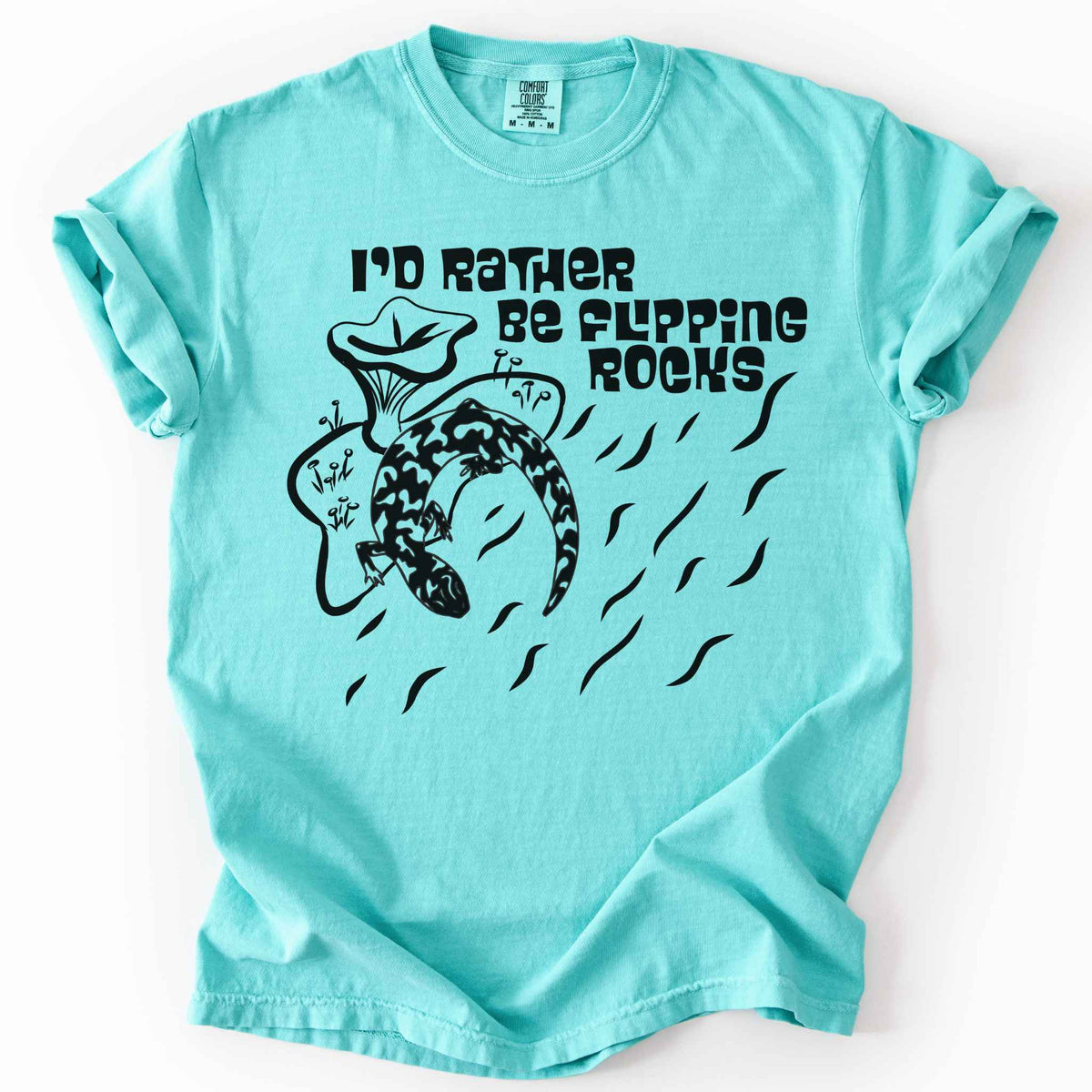 Chambray "I'd Rather Be Flipping Rocks" t-shirt on Comfort Colors tee, featuring a bold graphic of a curled salamander with mushrooms in a groovy retro font. Funny herpetology gift shirt for salamander hunters and amphibian enthusiasts.
