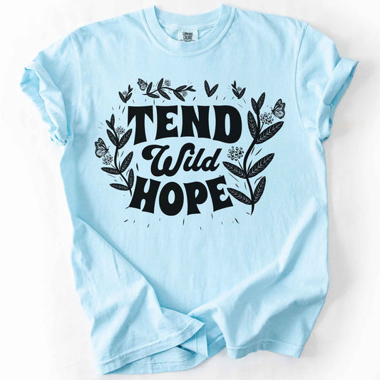 Chambray "Tend Wild Hope" t-shirt on Comfort Colors tee, featuring hand drawn butterflies and milkweed flowers framing bold lettering. Gardener and native plant gift shirt for pollinator conservation and nature lovers.
