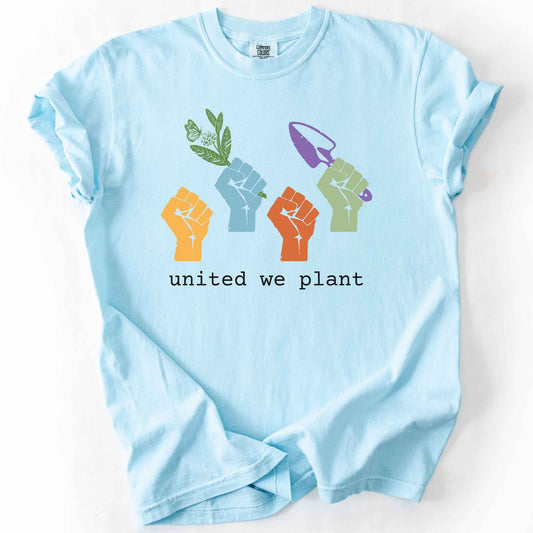 Chambray "United We Plant" t-shirt on Comfort Colors tee, featuring four colorful raised fists, one holding a plant sprig and another a garden trowel, above bold black text. Gardener and native plant gift shirt for community garden and conservation enthusiasts.