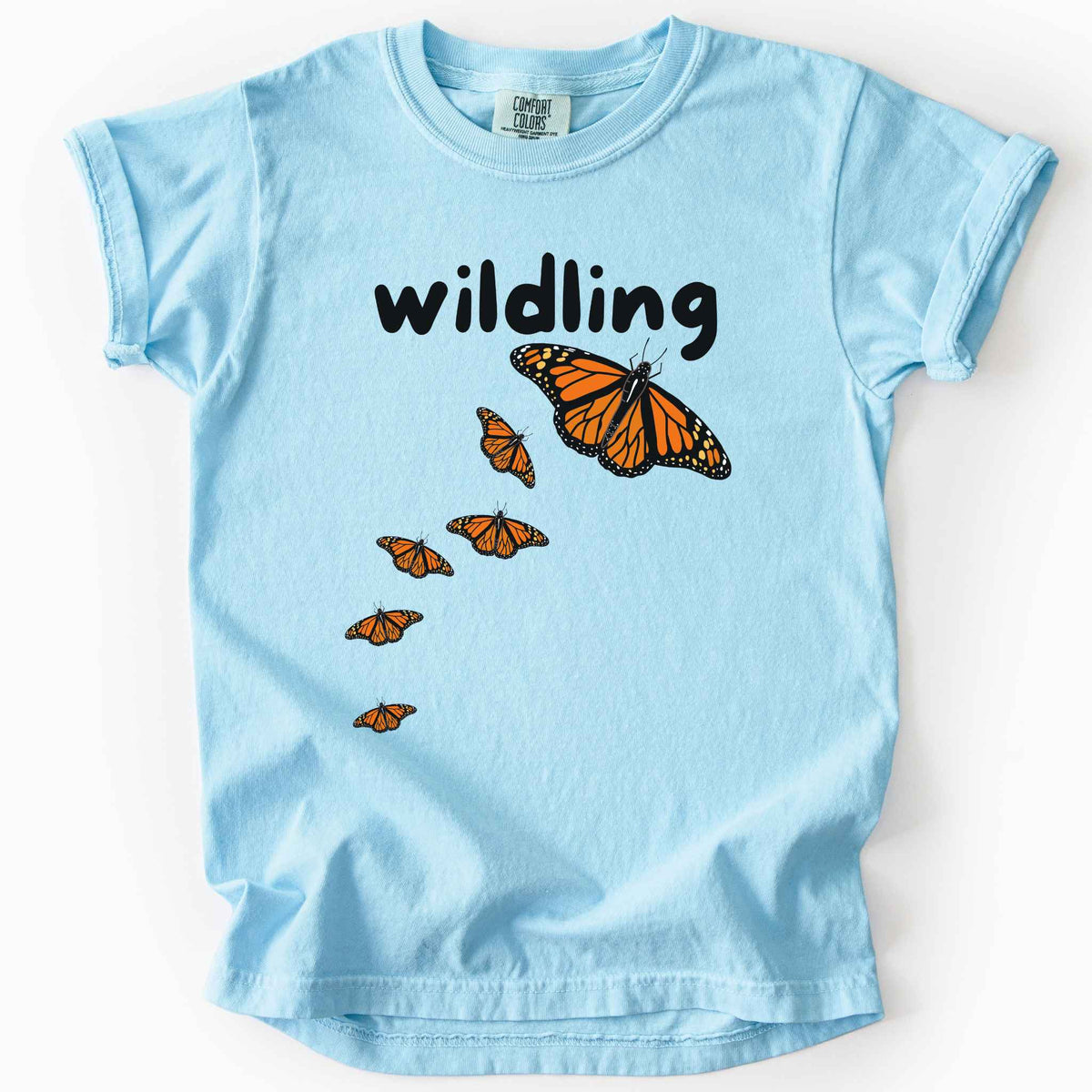 Chambray "Wildling" kids t-shirt on Comfort Colors Tee featuring six Monarch butterflies in an upward ascending pattern and bold black text. Nature inspired gift for kids and butterfly enthusiasts. 