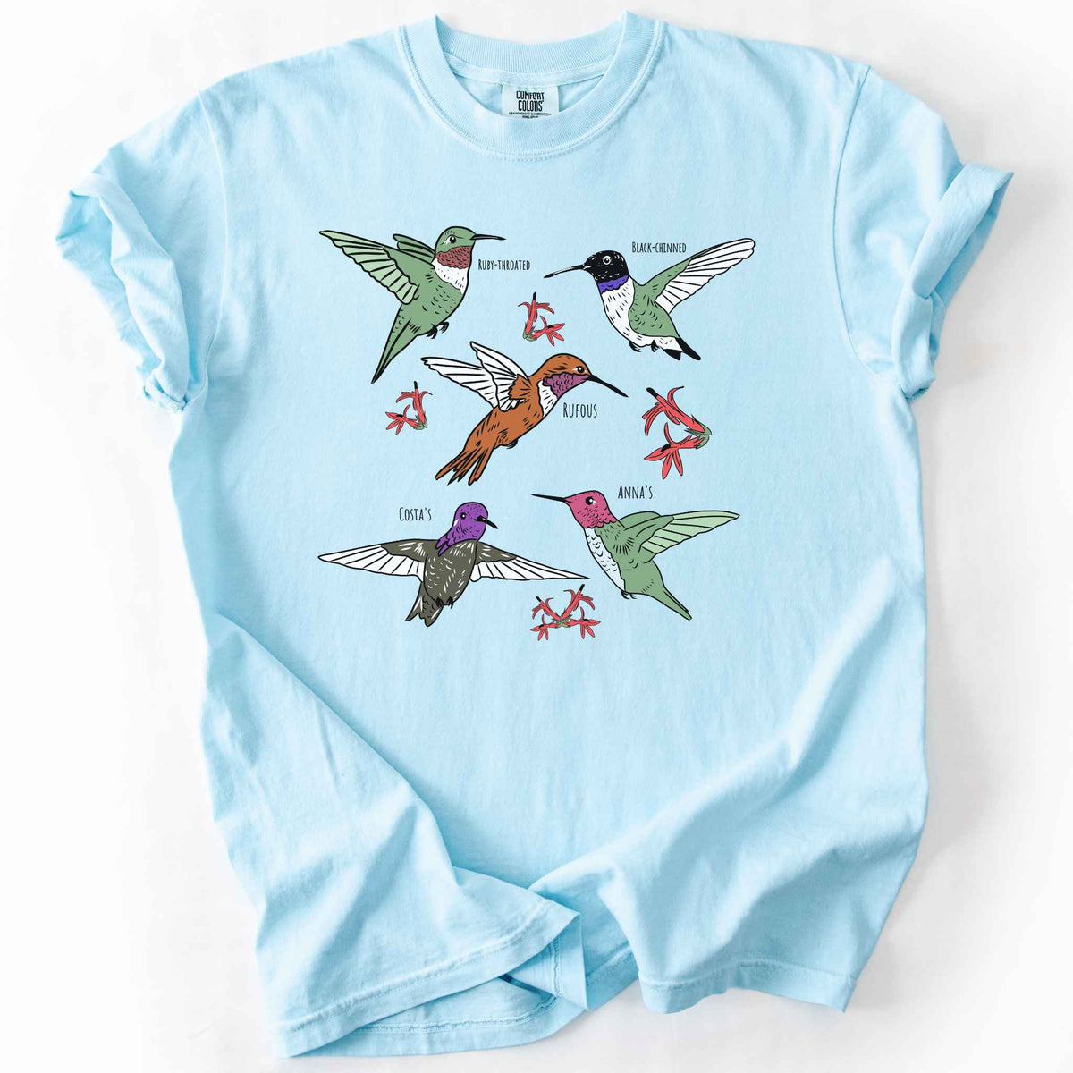 Chambray "hummingbirds" t-shirt on Comfort Colors tee, featuring five illustrated hummingbird species including Ruby Throated, Rufous, and Anna's, each labeled and shown among red flowers. Birdwatcher and hummingbird lover gift shirt for wildlife and nature enthusiasts.