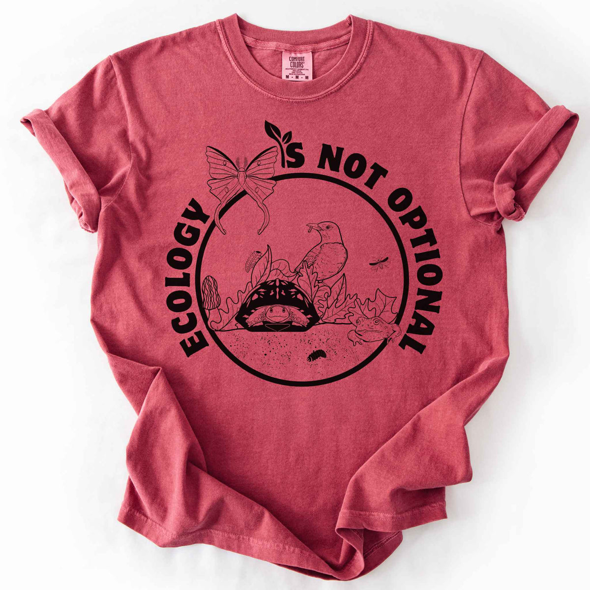Crimson "Ecology Is Not Optional" t-shirt on Comfort Colors tee, featuring a black circle badge with a box turtle, bird, luna moth, frog, and mushrooms in an ecosystem scene. Nature lover and biology gift shirt for ecologists and conservation enthusiasts.