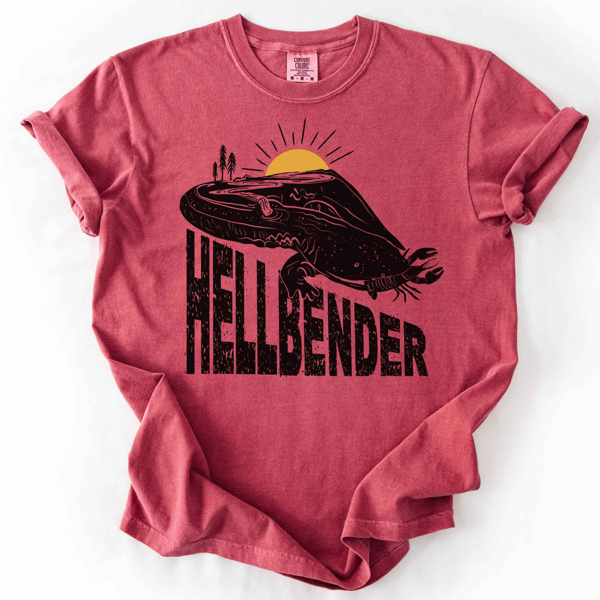Crimson "Hellbender a body of water" t-shirt on Comfort Colors tee, featuring a bold black graphic of a hellbender salamander eating a crayfish with a river landscape etched into its body. Amphibian and herpetology lover gift shirt for salamander and river conservation enthusiasts.