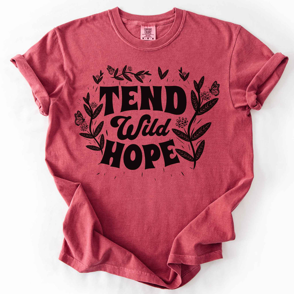 Crimson "Tend Wild Hope" t-shirt on Comfort Colors tee, featuring hand drawn butterflies and milkweed flowers framing bold lettering. Gardener and native plant gift shirt for pollinator conservation and nature lovers.