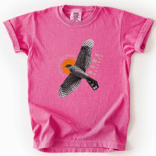 Crunchberry "Hawk Watcher, Eyes on the Skies" t-shirt on Comfort Colors tee, featuring a flying hawk graphic with spread wings against an orange sun design- birdwatching and raptor lover gift shirt for bird enthusiasts.