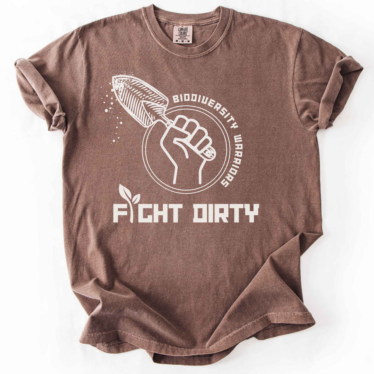 Espresso "Biodiversity Warriors, Fight Dirty" t-shirt on Comfort Colors tee, featuring a raised fist gripping a garden trowel in a circular badge design. Gardener and conservation lover gift shirt for native plant and biodiversity enthusiasts.