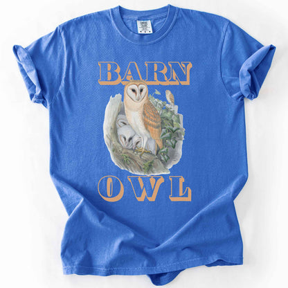 Flo Blue "Barn Owl" t-shirt on Comfort Colors tee, featuring a detailed graphic of a barn owl with owlets nestled in a tree hollow with ivy, in tan bold lettering. Birdwatcher and owl lover gift shirt for wildlife and nature enthusiasts.