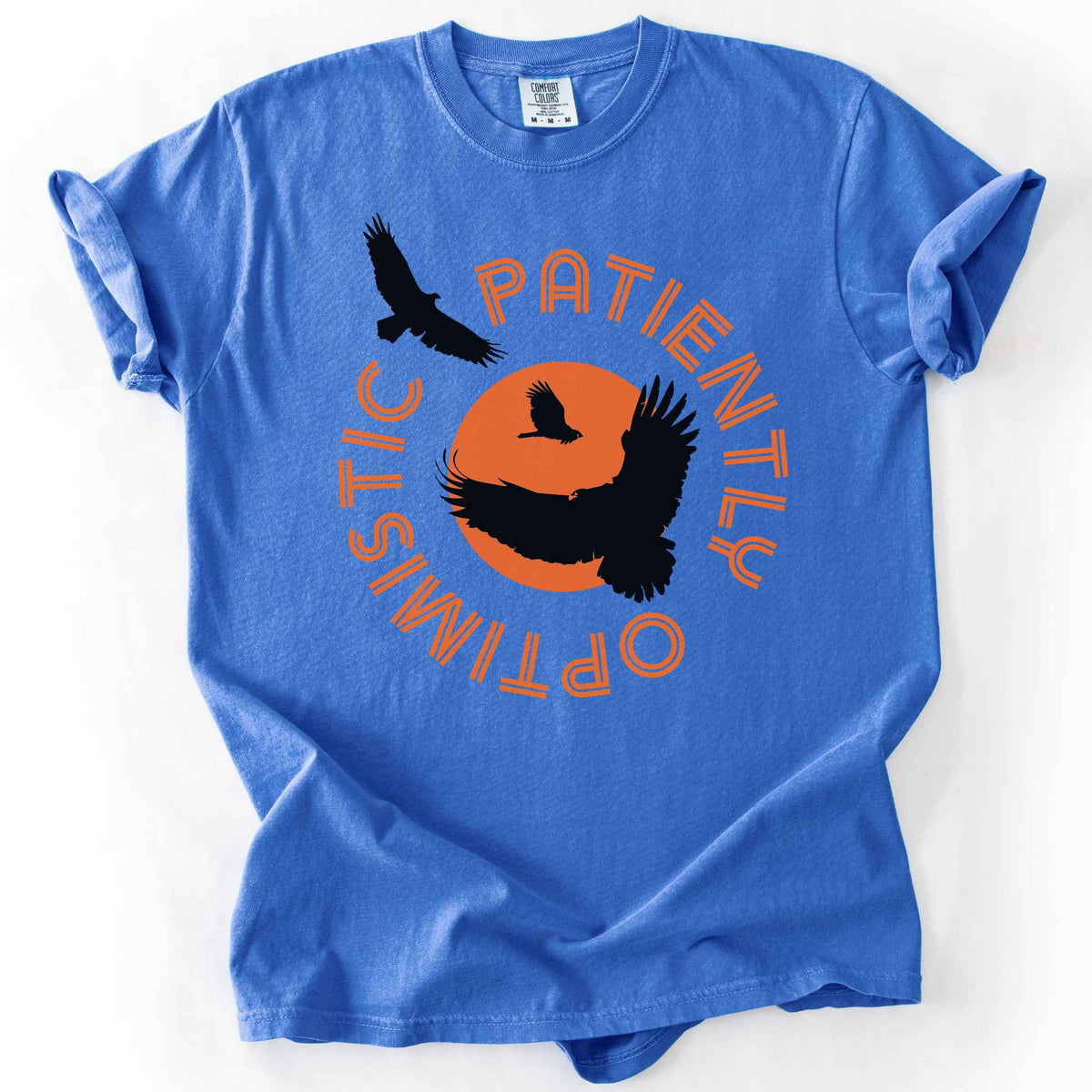 Flo blue "Patiently optimistic turkey vulture" t-shirt on comfort colors tee. Silhouette turkey vulture graphics against an orange sun surrounded by curved text. Bird lover and wildlife enthusiast gift. 