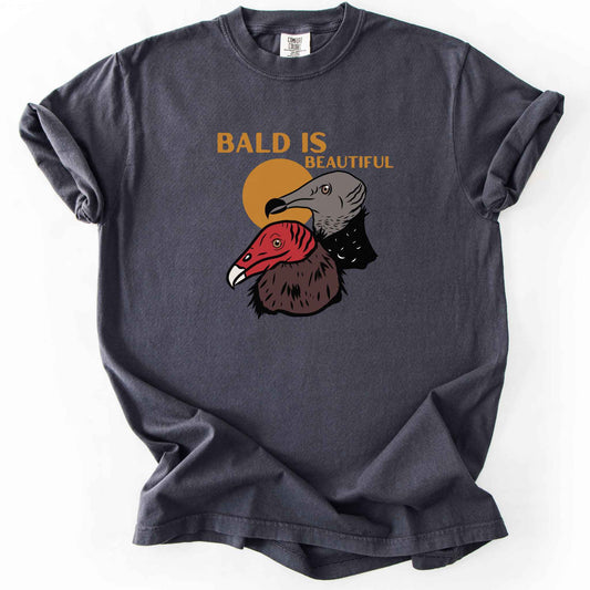Graphite "Bald Is Beautiful" t-shirt on Comfort Colors tee, featuring illustrated turkey vulture and black vulture heads with orange retro sun and orange lettering. Funny birdwatcher gift shirt for vulture and scavenger lovers.