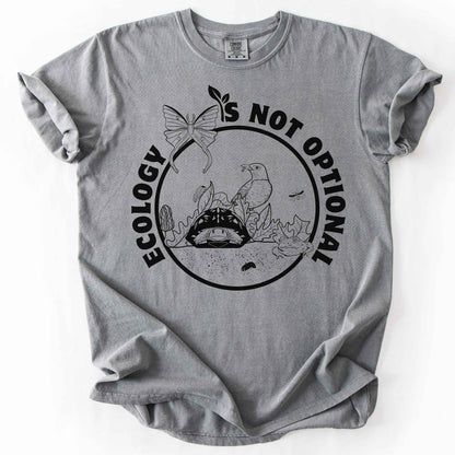 Grey "Ecology Is Not Optional" t-shirt on Comfort Colors tee, featuring a black circle badge with a box turtle, bird, luna moth, frog, and mushrooms in an ecosystem scene. Nature lover and biology gift shirt for ecologists and conservation enthusiasts.