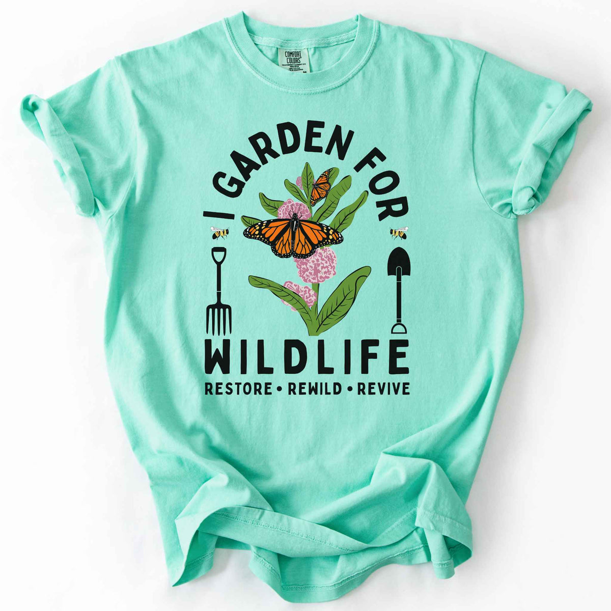 Island Reef "I Garden for Wildlife, Restore, Rewild, Revive" t-shirt on Comfort Colors tee, featuring monarch butterflies and bees on milkweed flowers flanked by garden tools in orange and gold tones. Gardener and native plant gift shirt for pollinator conservation fans.