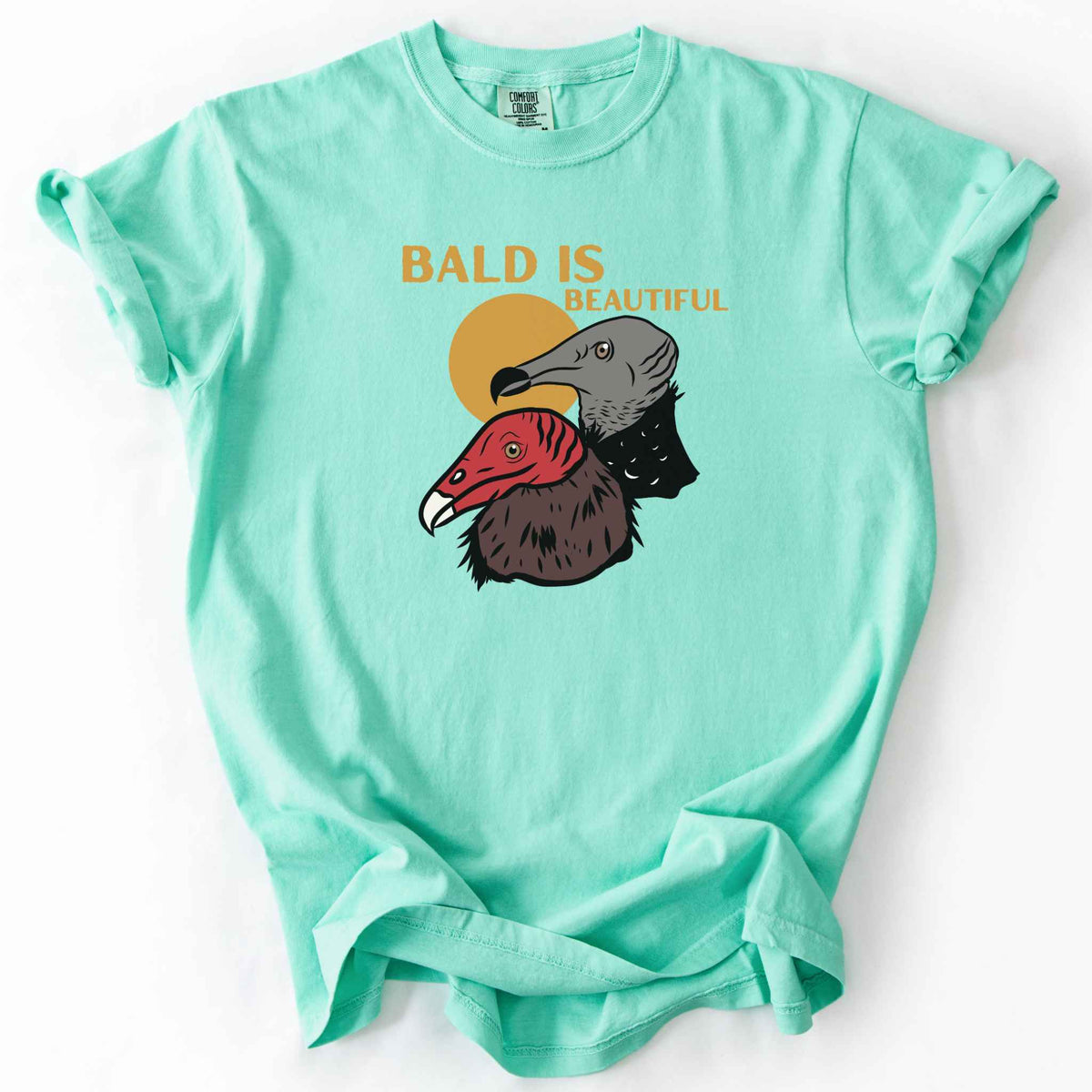 Island reef "Bald Is Beautiful" t-shirt on Comfort Colors tee, featuring illustrated turkey vulture and black vulture heads with orange retro sun and orange lettering. Funny birdwatcher gift shirt for vulture and scavenger lovers.