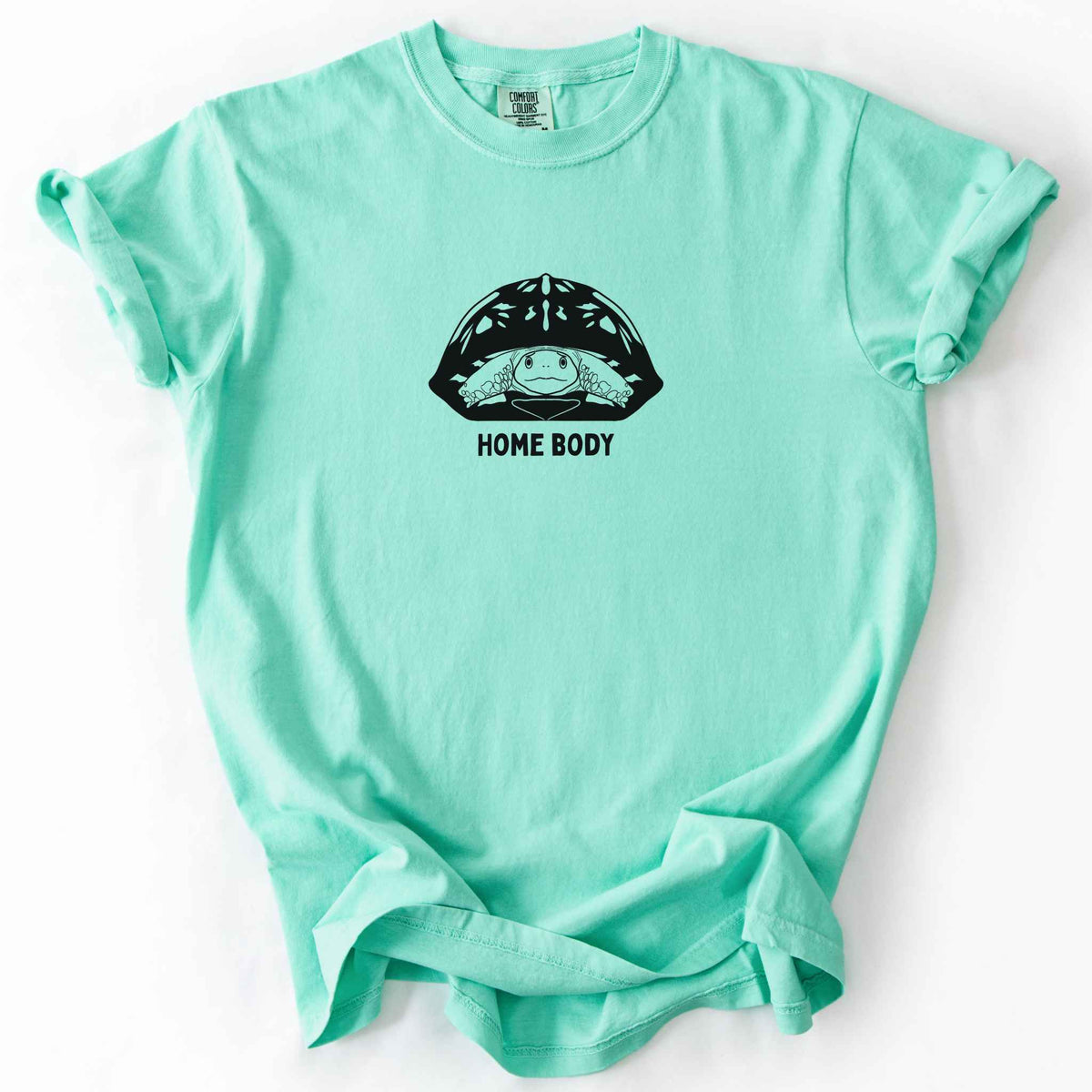 Island reef "Home Body" t-shirt on Comfort Colors tee, featuring a bold black graphic of a turtle peeking out from its shell above simple lettering. Funny turtle lover gift shirt for introverts and reptile enthusiasts.