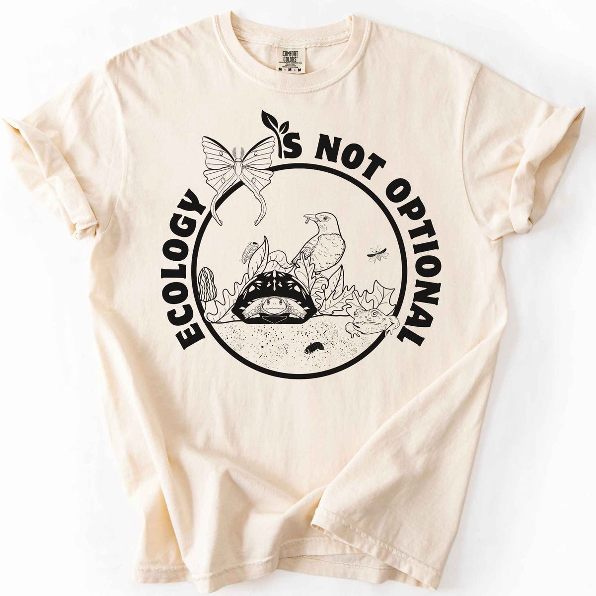 Ivory "Ecology Is Not Optional" t-shirt on Comfort Colors tee, featuring a black circle badge with a box turtle, bird, luna moth, frog, and mushrooms in an ecosystem scene. Nature lover and biology gift shirt for ecologists and conservation enthusiasts.