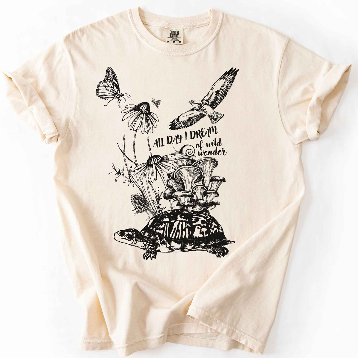 Ivory "Fauna and Flora" t-shirt on Comfort Colors tee, featuring the words "all day I dream of wild wonder", and a nature scene in black line art style with a box turtle, mushrooms, wildflowers, a hawk, a butterfly, and a snail. Nature lover and forager gift shirt for cottagecore and wildlife enthusiasts.