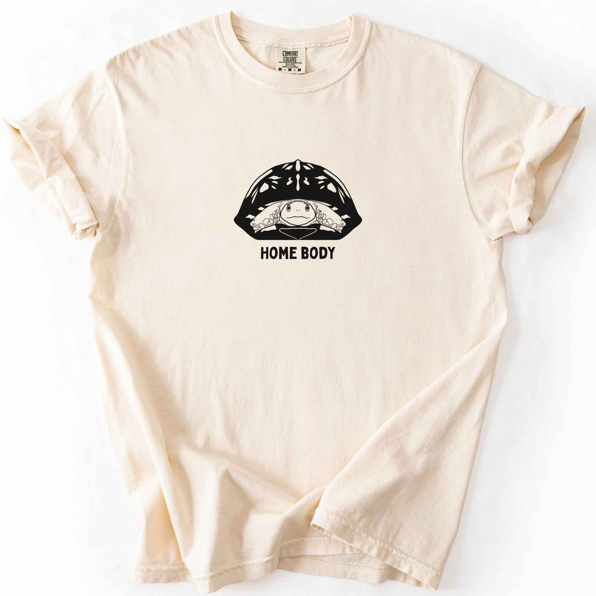 Ivory "Home Body" t-shirt on Comfort Colors tee, featuring a bold black graphic of a turtle peeking out from its shell above simple lettering. Funny turtle lover gift shirt for introverts and reptile enthusiasts.