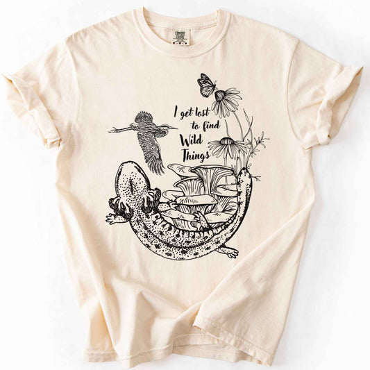 Ivory "I Get Lost to Find Wild Things" t-shirt on Comfort Colors tee, featuring a curled mudpuppy salamander, heron, mushrooms, monarch and coneflowers line art style. Nature lover and hiking gift shirt for salamander and wildlife enthusiasts.