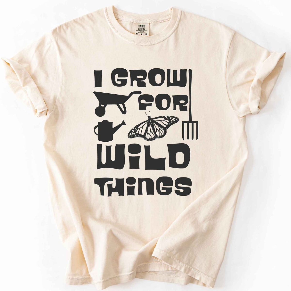 Ivory "I Grow for Wild Things" t-shirt on Comfort Colors tee, featuring a monarch butterfly with garden tool icons and bold black lettering text. Gardener and native plant gift shirt for pollinator conservation fans.