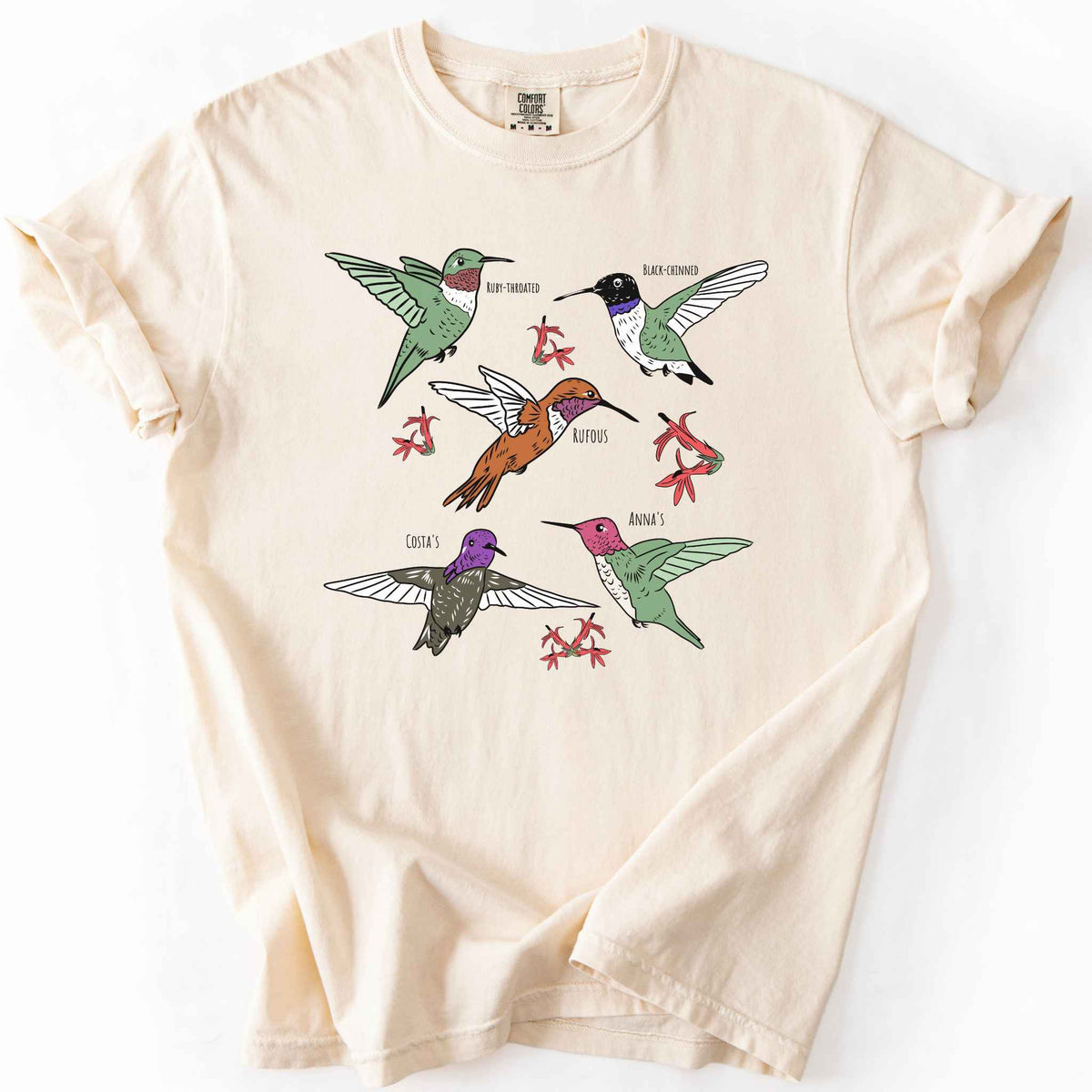 Ivory "hummingbirds" t-shirt on Comfort Colors tee, featuring five illustrated hummingbird species including Ruby Throated, Rufous, and Anna's, each labeled and shown among red flowers. Birdwatcher and hummingbird lover gift shirt for wildlife and nature enthusiasts.