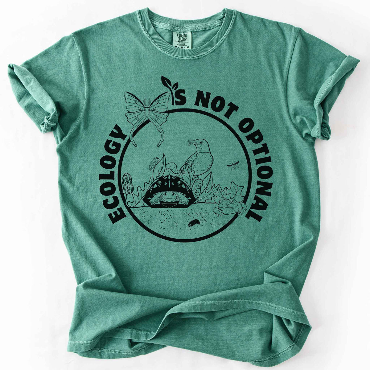 Light Green "Ecology Is Not Optional" t-shirt on Comfort Colors tee, featuring a black circle badge with a box turtle, bird, luna moth, frog, and mushrooms in an ecosystem scene. Nature lover and biology gift shirt for ecologists and conservation enthusiasts.