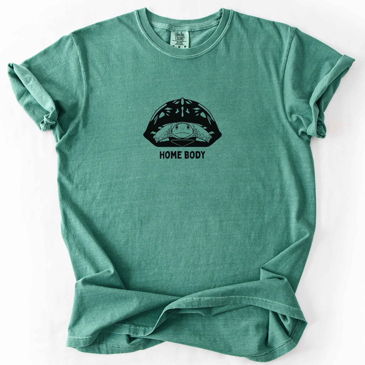 Light green "Home Body" t-shirt on Comfort Colors tee, featuring a bold black graphic of a turtle peeking out from its shell above simple lettering. Funny turtle lover gift shirt for introverts and reptile enthusiasts.