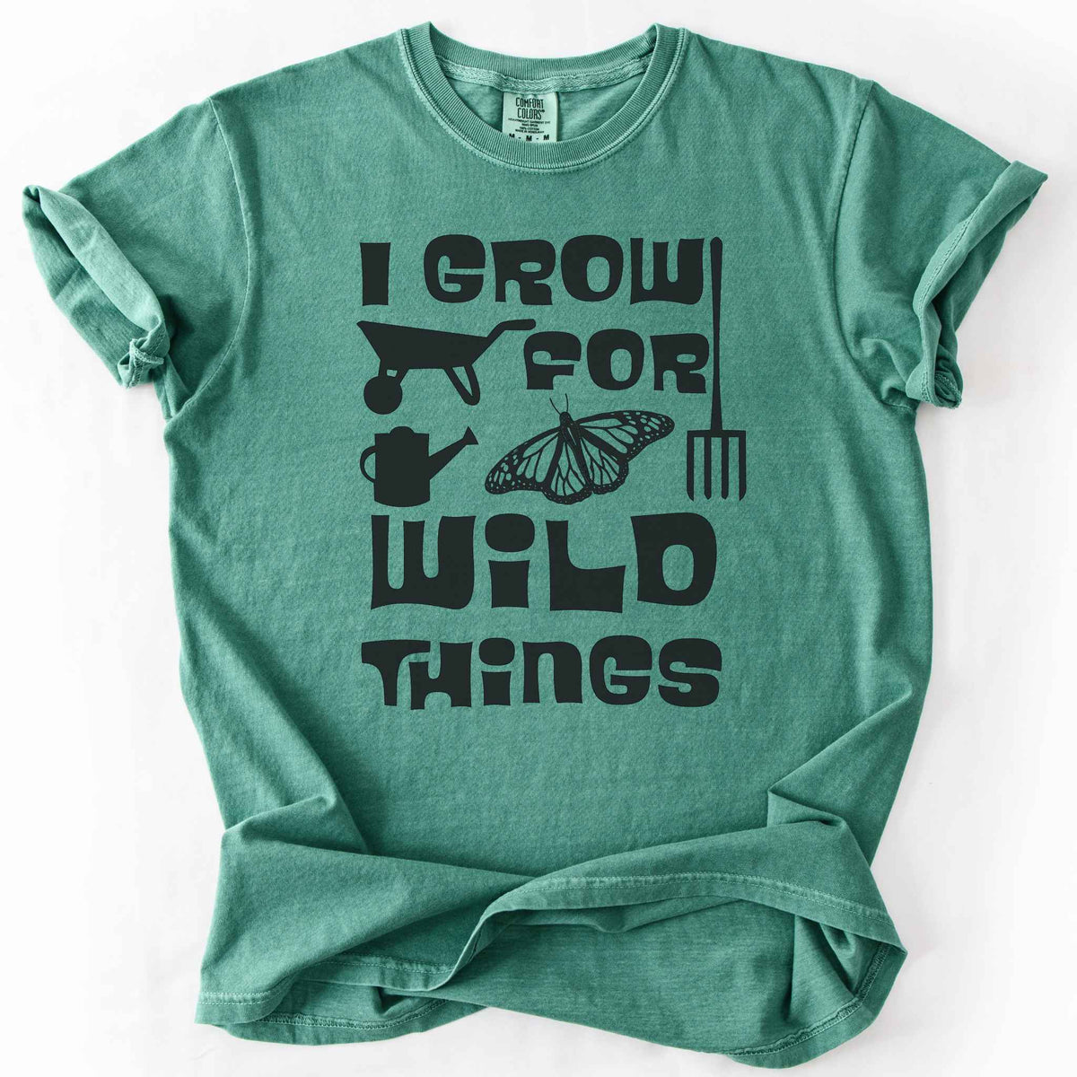 Light green "I Grow for Wild Things" t-shirt on Comfort Colors tee, featuring a monarch butterfly with garden tool icons and bold black lettering text. Gardener and native plant gift shirt for pollinator conservation fans.