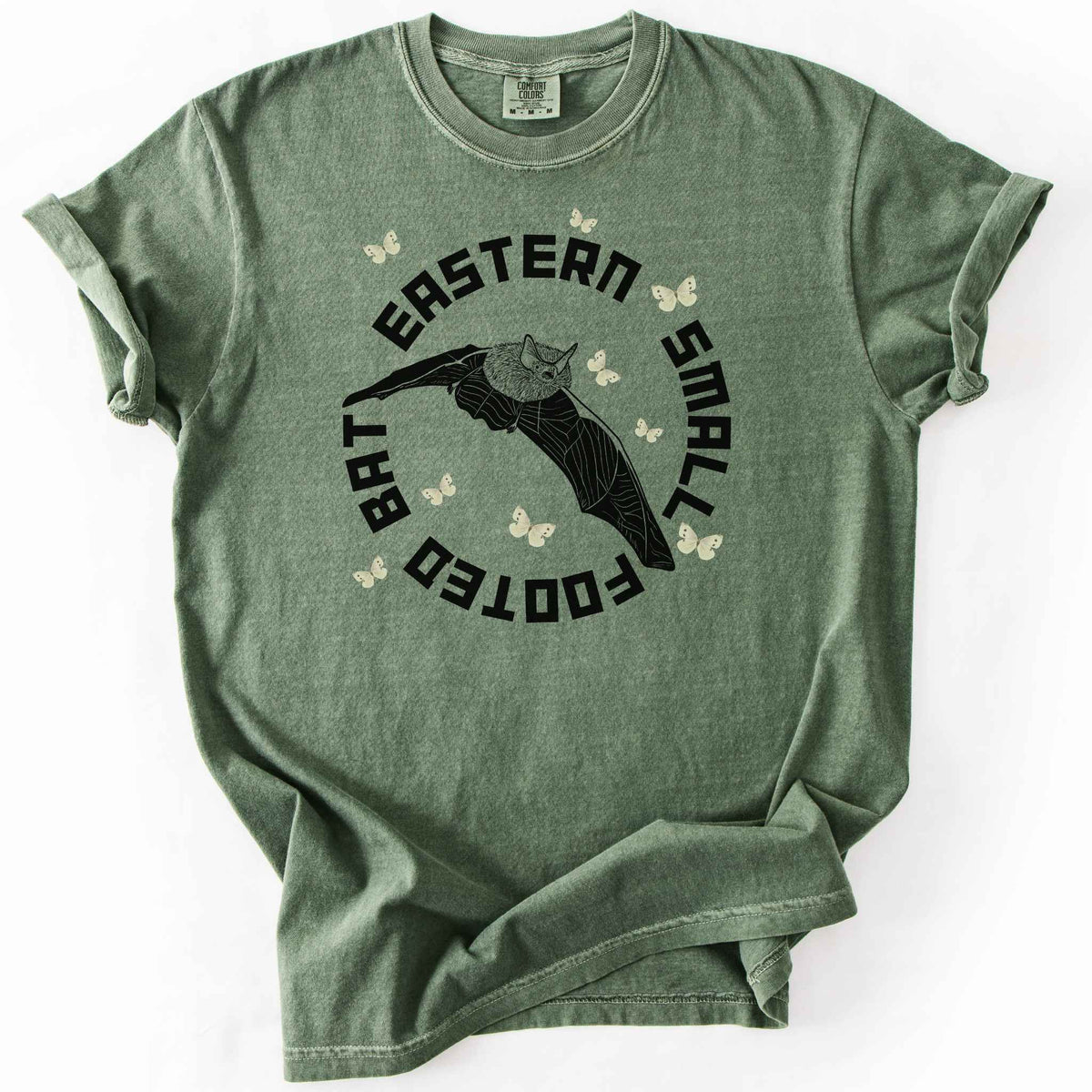 Moss "Eastern Small Footed Bat" t-shirt on Comfort Colors tee, featuring a black illustration of a flying bat surrounded by pale moths in a circular badge design. Bat lover and wildlife gift shirt for nocturnal animal and nature enthusiasts.