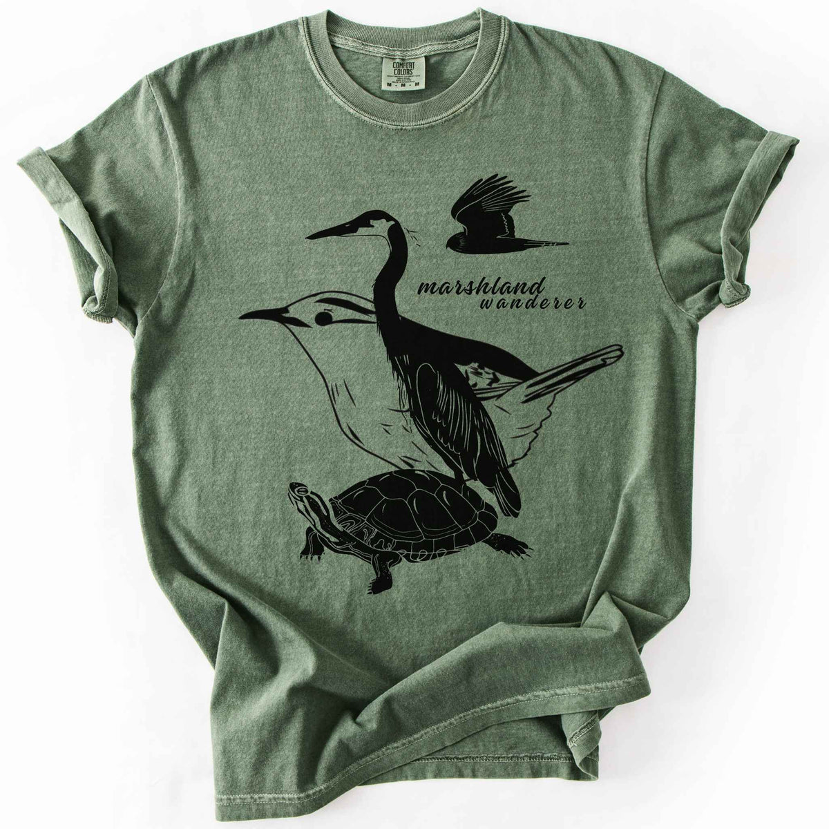 Moss "Marshland Wanderer" t-shirt on Comfort Colors tee, featuring a surreal black line art design blending a heron, marsh wren, turtle, and marsh harrier into one flowing wetland scene. Nature lover and wetland conservation gift shirt for birdwatching and wildlife enthusiasts.
