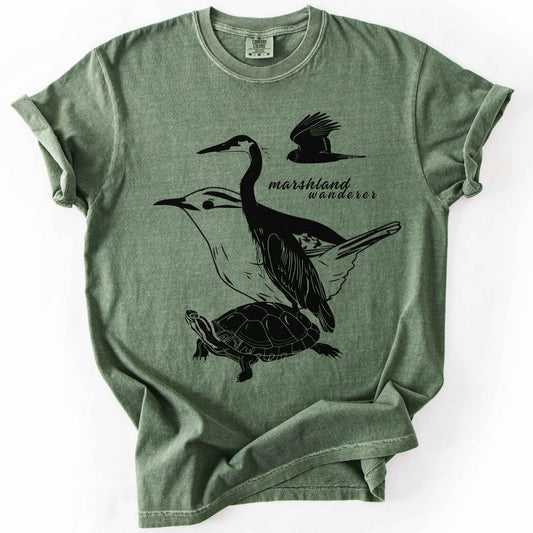 Moss "Marshland Wanderer" t-shirt on Comfort Colors tee, featuring a surreal black line art design blending a heron, marsh wren, turtle, and marsh harrier into one flowing wetland scene. Nature lover and wetland conservation gift shirt for birdwatching and wildlife enthusiasts.