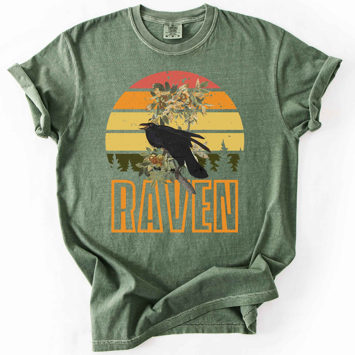 Moss "Raven" t-shirt on Comfort Colors tee, featuring a raven perched on a branch against a retro sunset sunburst design with bold orange text. Bird lover and wildlife gift shirt for corvid and nature enthusiasts.