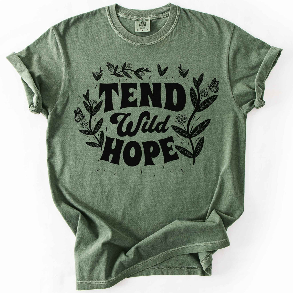 Moss "Tend Wild Hope" t-shirt on Comfort Colors tee, featuring hand drawn butterflies and milkweed flowers framing bold lettering. Gardener and native plant gift shirt for pollinator conservation and nature lovers.