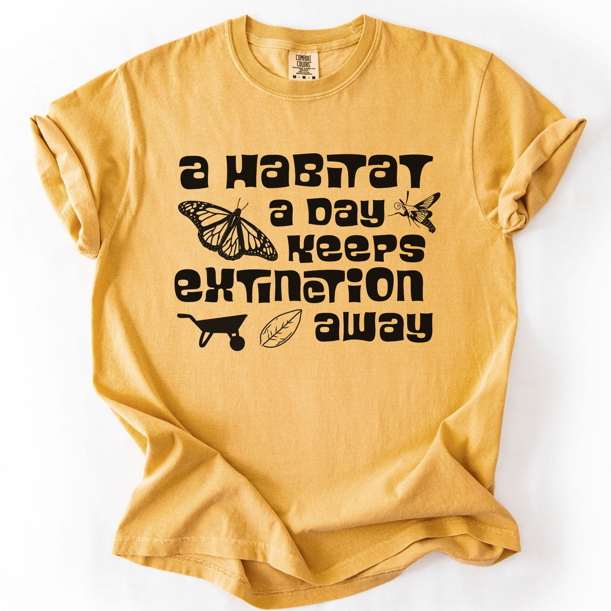 Mustard "A Habitat a Day Keeps Extinction Away" t-shirt on Comfort Colors tee, featuring a monarch butterfly, clearwing moth, wheelbarrow, and leaf icon with bold black lettering. Gardener and conservation gift shirt for native plant and pollinator enthusiasts.