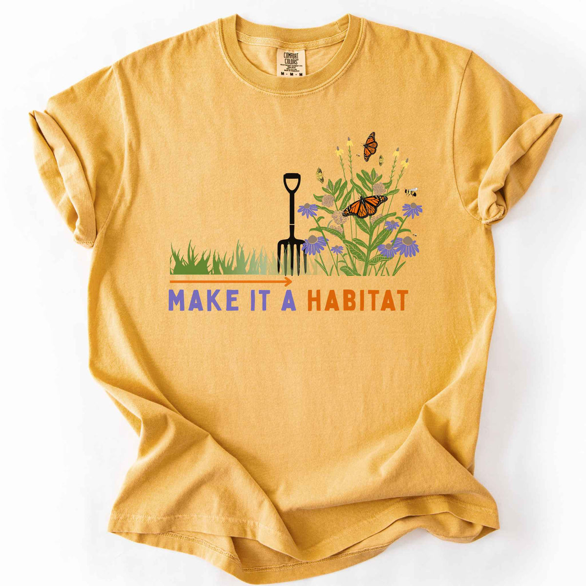 Mustard "Make It a Habitat" t-shirt on Comfort Colors tee, featuring a garden fork beside coneflowers and milkweed with monarch butterflies and bees, transforming grass into wildflowers. Gardener and native plant gift shirt for pollinator conservation fans.