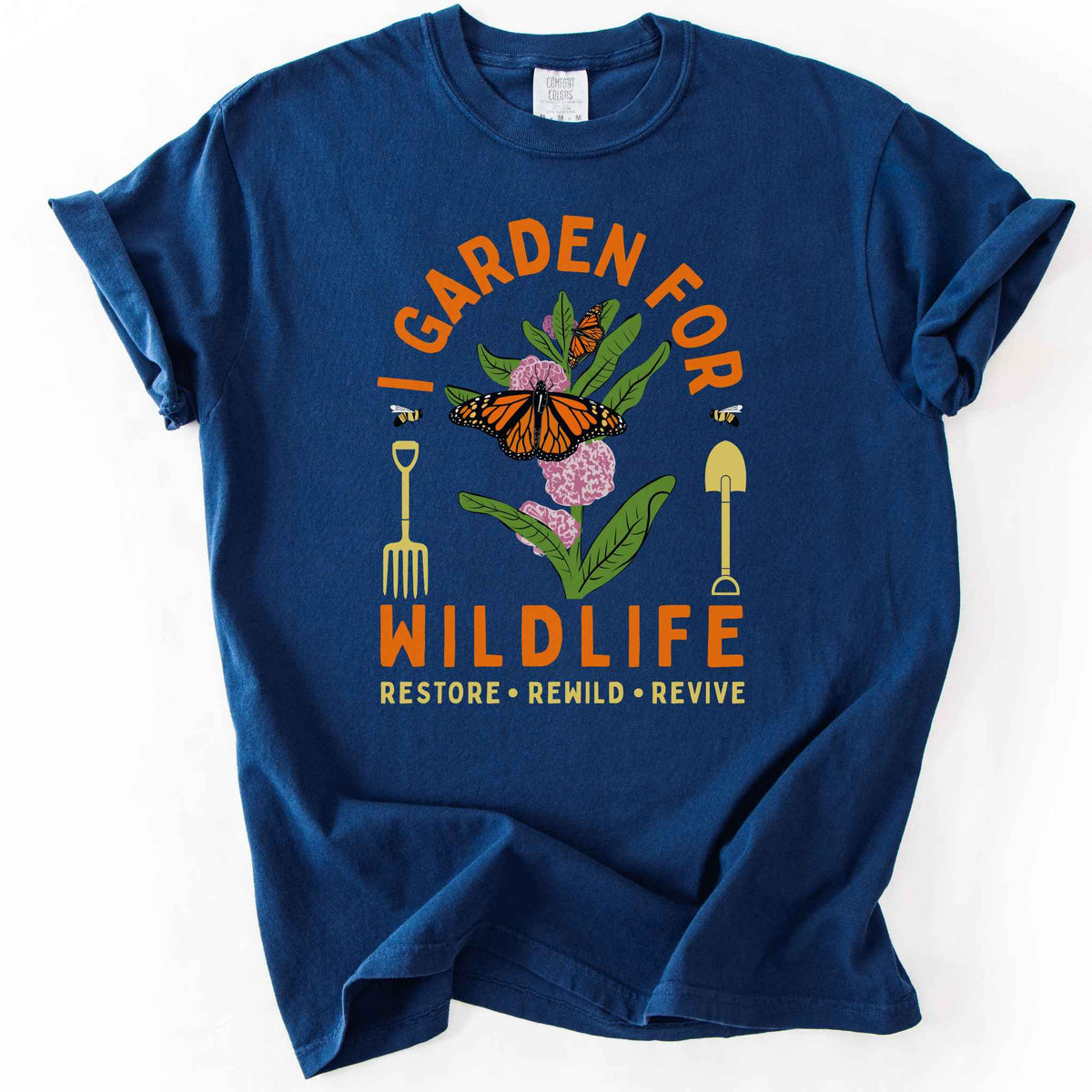 Navy "I Garden for Wildlife, Restore, Rewild, Revive" t-shirt on Comfort Colors tee, featuring monarch butterflies and bees on milkweed flowers flanked by garden tools in orange and gold tones. Gardener and native plant gift shirt for pollinator conservation fans.