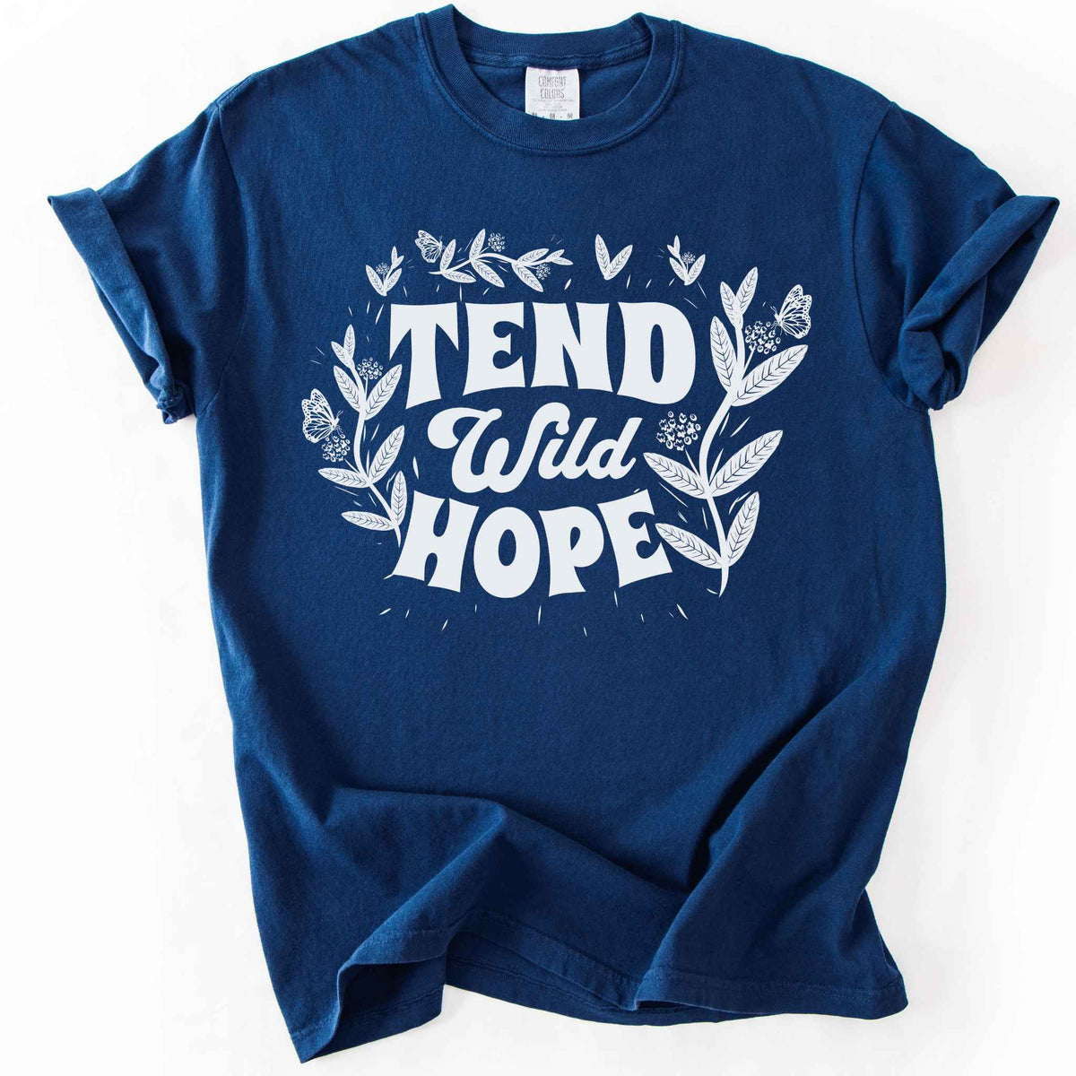Navy "Tend Wild Hope" t-shirt on Comfort Colors tee, featuring hand drawn butterflies and milkweed flowers framing bold lettering. Gardener and native plant gift shirt for pollinator conservation and nature lovers.