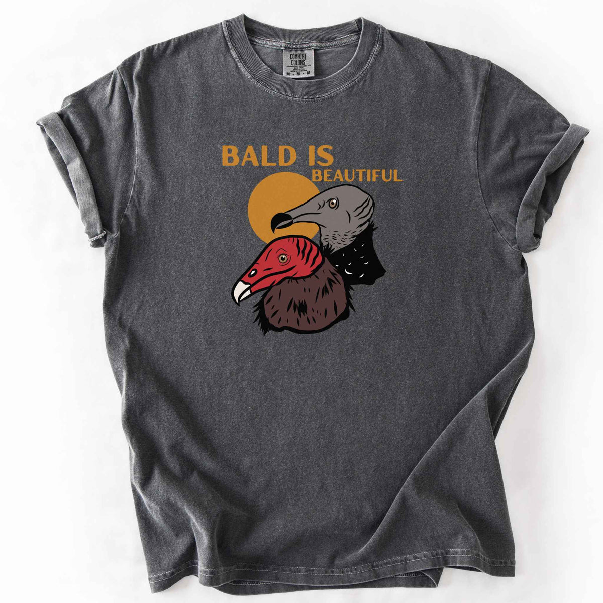 Pepper "Bald Is Beautiful" t-shirt on Comfort Colors tee, featuring illustrated turkey vulture and black vulture heads with orange retro sun and orange lettering. Funny birdwatcher gift shirt for vulture and scavenger lovers.