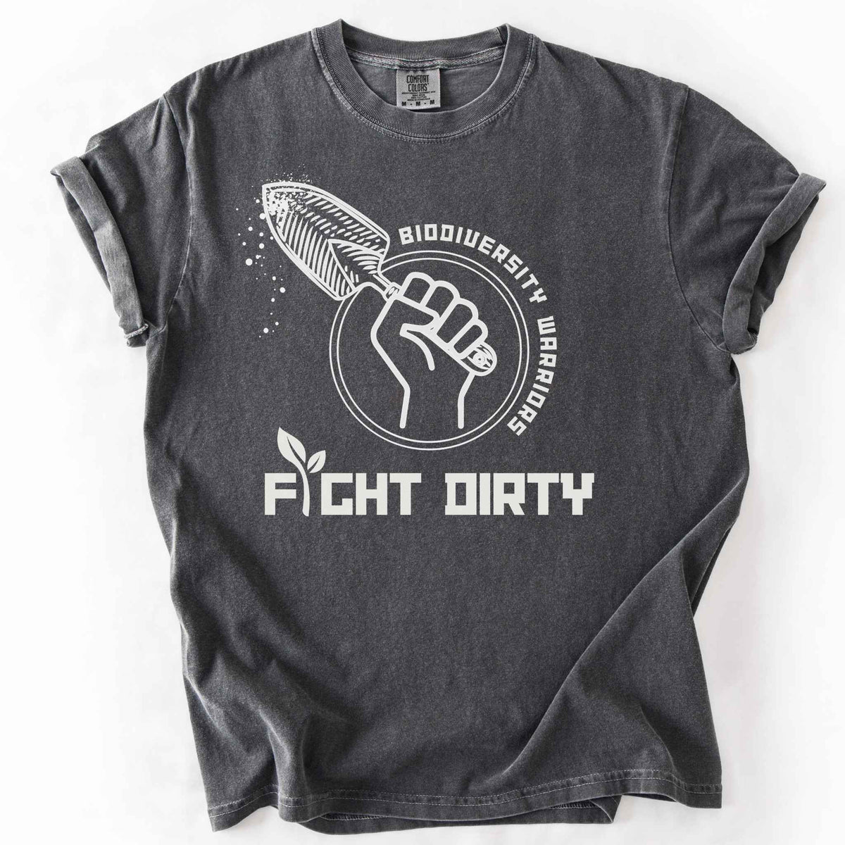 Pepper "Biodiversity Warriors, Fight Dirty" t-shirt on Comfort Colors tee, featuring a raised fist gripping a garden trowel in a circular badge design. Gardener and conservation lover gift shirt for native plant and biodiversity enthusiasts.
