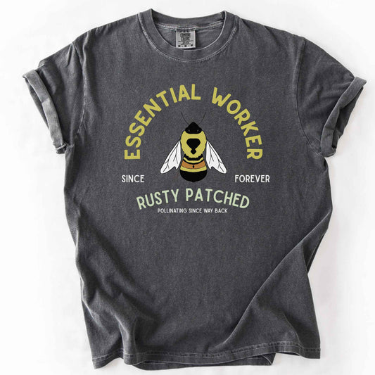 Pepper "Essential Worker, Rusty Patched, Pollinating Since Way Back" t-shirt on Comfort Colors tee, featuring an illustrated bumblebee in a circular design. Funny bee lover gift shirt for pollinator and rusty patched bumblebee conservation fans.