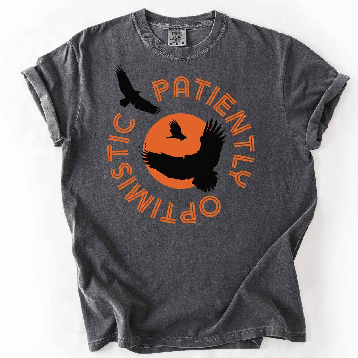 Pepper "Patiently optimistic turkey vulture" t-shirt on comfort colors tee. Silhouette turkey vulture graphics against an orange sun surrounded by curved text. Bird lover and wildlife enthusiast gift. 