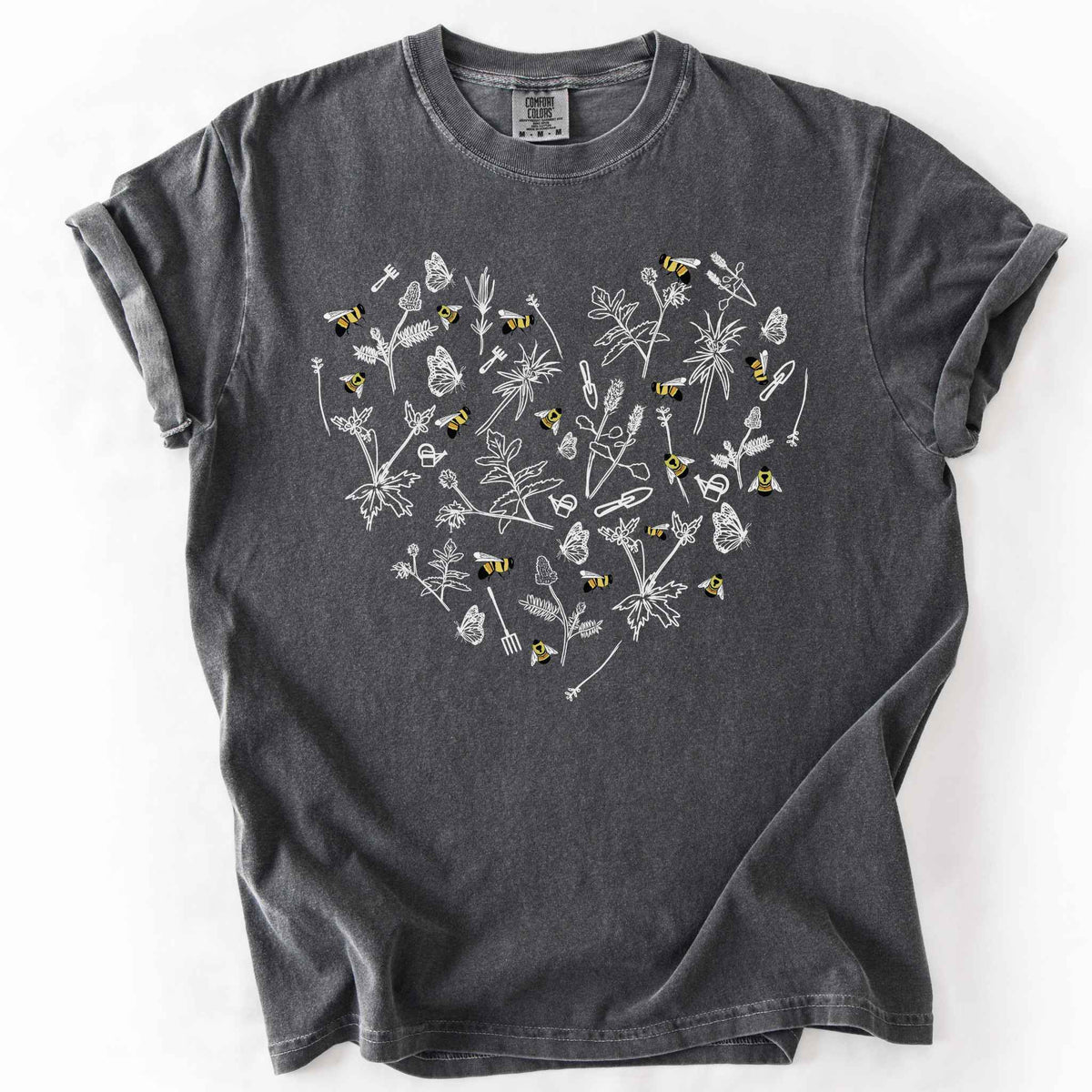 Pepper "Rusty Patch Bumblebee" t-shirt on Comfort Colors tee, featuring a heart shaped arrangement of hand-drawn white wildflowers, garden tools, butterflies, and colorful bees. Gardener and pollinator lover gift shirt for bee conservation and nature enthusiasts.