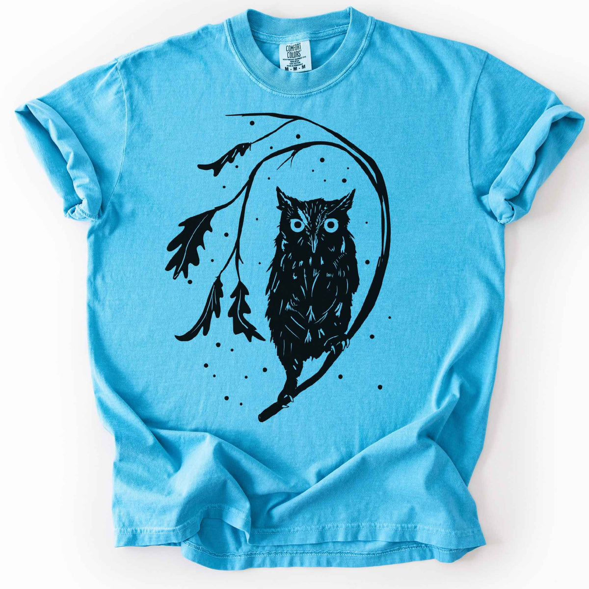 Sapphire "Eastern Screech starry night" owl t-shirt on Comfort Colors tee, featuring a bold black illustration of a screech owl perched on a leafy branch with scattered dots for stars. Birdwatcher and owl lover gift shirt for wildlife and nature enthusiasts.