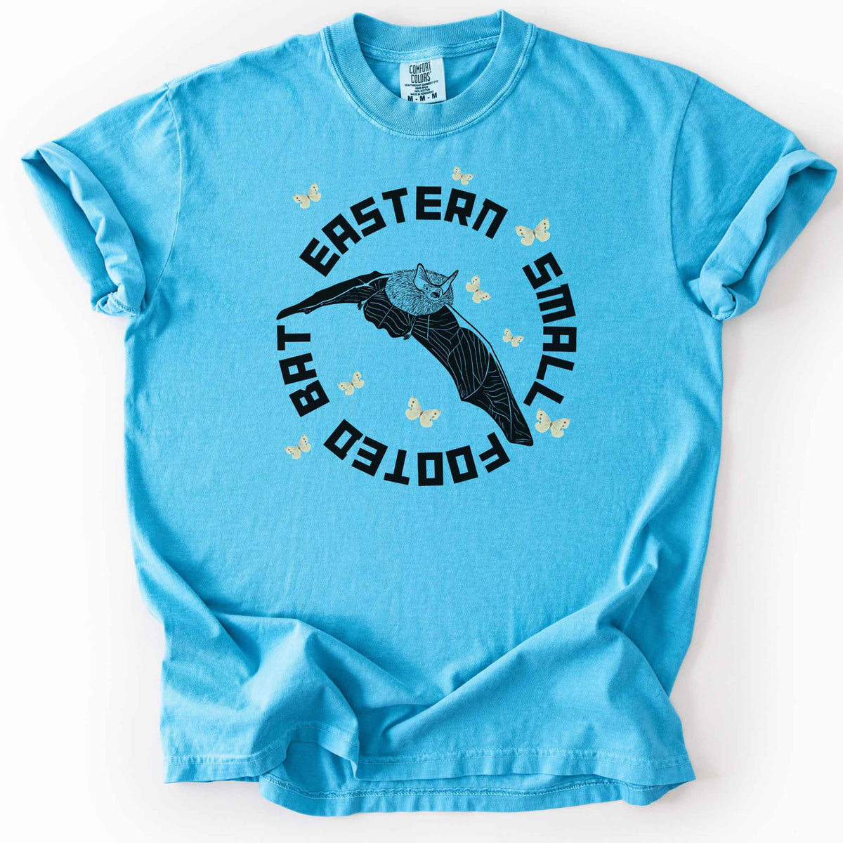 Sapphire "Eastern Small Footed Bat" t-shirt on Comfort Colors tee, featuring a black illustration of a flying bat surrounded by pale moths in a circular badge design. Bat lover and wildlife gift shirt for nocturnal animal and nature enthusiasts.