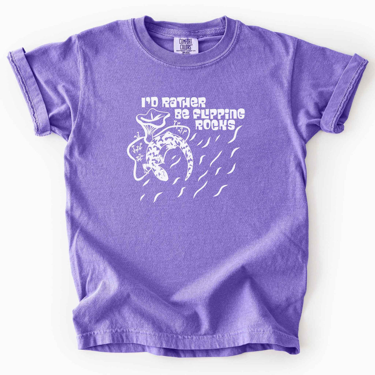 Violet "I'd Rather Be Flipping Rocks" kids t-shirt on Comfort Colors tee, featuring a bold graphic of a curled salamander with mushrooms in a groovy retro font. Funny herpetology gift shirt for salamander hunters and amphibian enthusiasts.