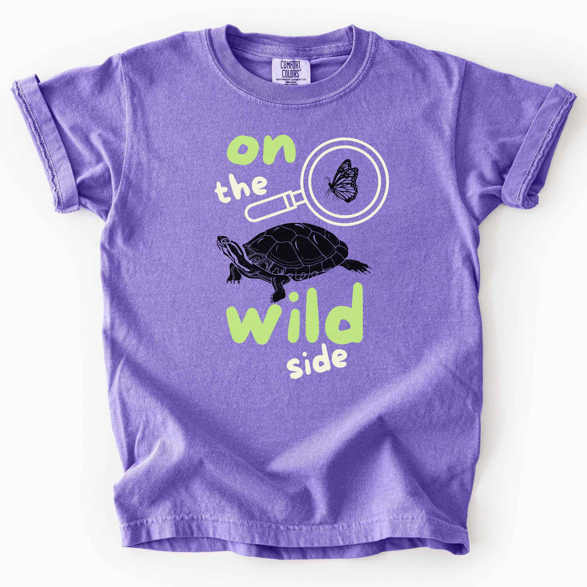 Violet "On the wild side" kids t-shirt on Comfort Colors tee featuring a butterfly in a magnifying glass and painted turtle graphic with bold and playful text. Nature lover kids shirt for wildlife and exploration enthusiasts. 